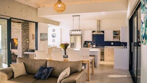 Een moderne woonkamer met een bank, eettafel en stoelen. Er is een keuken met kasten en een koelkast.