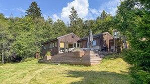A cabin with a wooden exterior, a deck, and a large window overlooking a forested area. - 2 bedroom beautiful home in Gressvik (Gressvik)