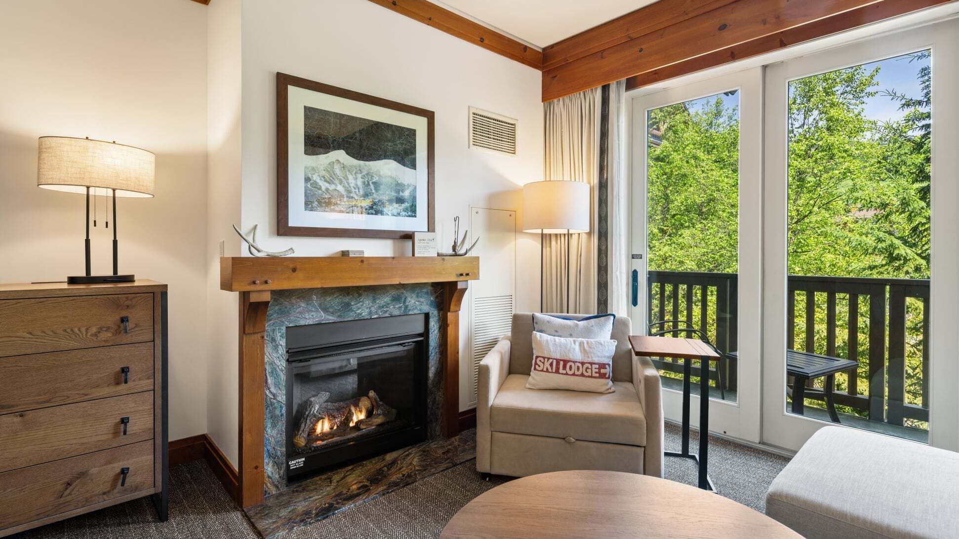 A cozy room with a fireplace, a sofa, a table, and a balcony with a view of trees.