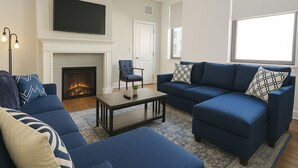 Ein Wohnzimmer mit Kamin, zwei Sofas, einem Couchtisch und einem an der Wand befestigten Fernseher.