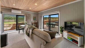 A modern living room with a large TV, comfortable seating, and a view of a landscaped outdoor area.