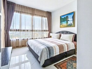 A bedroom with a bed, curtains, a painting, and a rug. - Zire Wonamat - Luxury Large One BR Seaview Apartment, Pattay Beach (Pattaya)