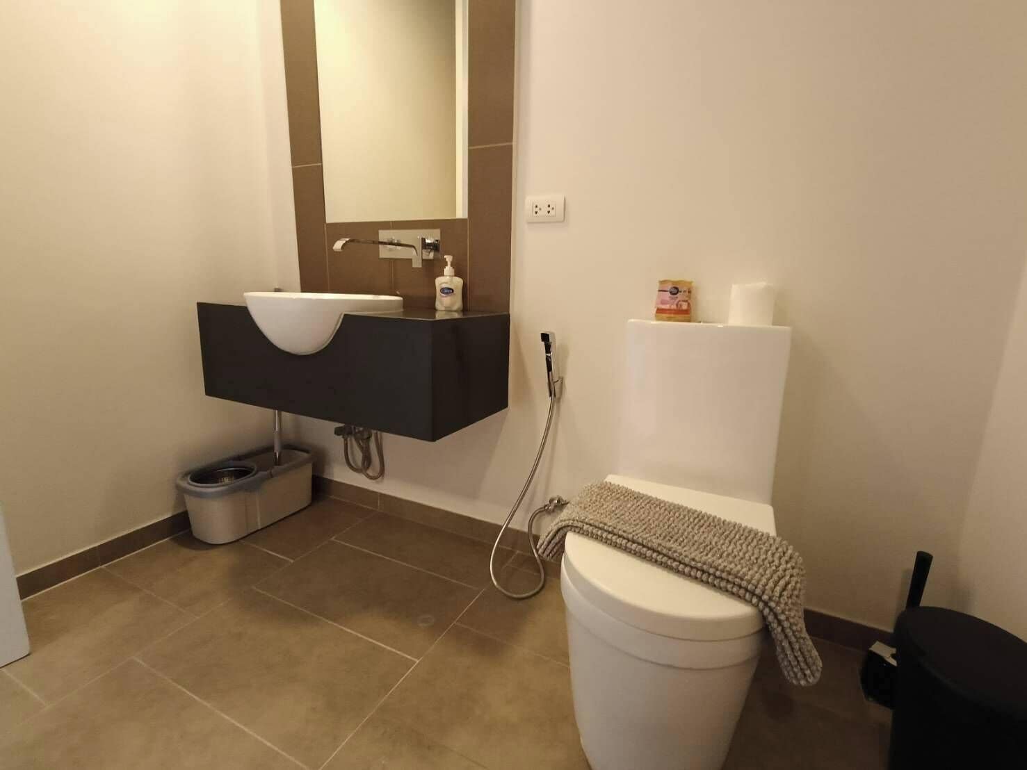 A modern bathroom with a white toilet, a black sink with a mirror above it, and a shower head.