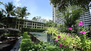 Un patio de hotel con piscina, palmeras y un edificio con amplios ventanales.