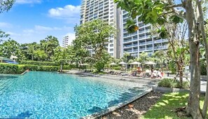 A swimming pool with lounge chairs and umbrellas, surrounded by greenery and tall buildings. - Zire Wonamat - Luxury Large One BR Seaview Apartment, Pattay Beach (Pattaya)