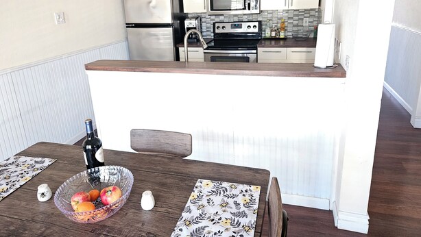 Una cocina compacta con armarios blancos, un refrigerador de acero inoxidable, un microondas y una estufa.