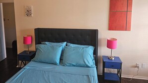 Un dormitorio con una cama, dos mesitas de noche, dos lámparas, un reloj de pared y un cuadro.