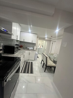 A modern kitchen with white cabinets, a microwave, a stove, and a dining area with a table and chairs. -  Cozy  bedroom Unit in Boston. (Boston)