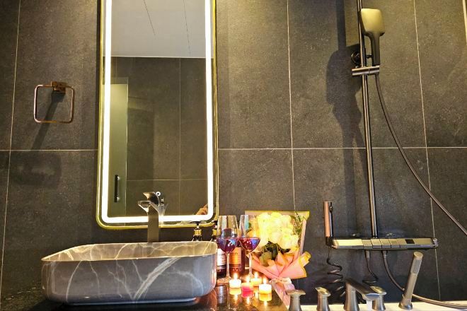 A modern bathroom with a large mirror, a marble sink, and a shower area.