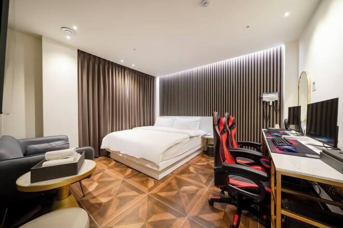 Una habitación de hotel con cama, escritorio con computadora, silla, sofá y una pequeña mesa redonda.