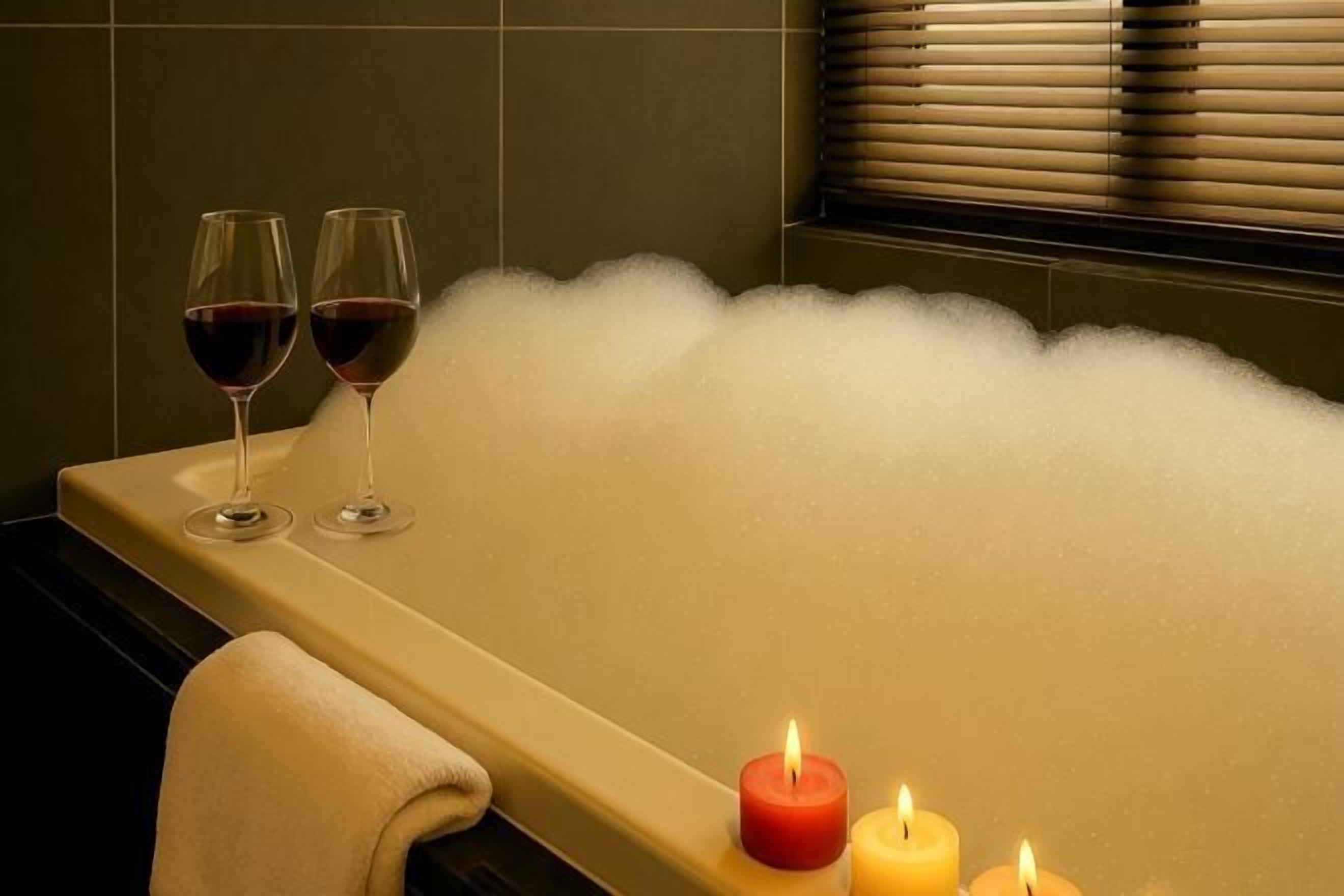 Uma banheira com dois copos de vinho tinto e duas velas acesas.
