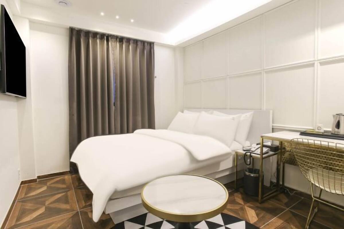 Una habitación de hotel moderna con una cama grande, una mesita redonda pequeña, un escritorio con silla y un televisor montado en la pared.
