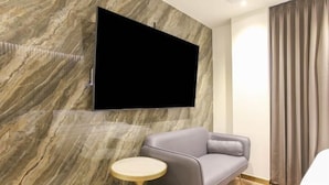 Una habitación moderna con televisor montado, un sofá gris, una mesita redonda y una cortina.
