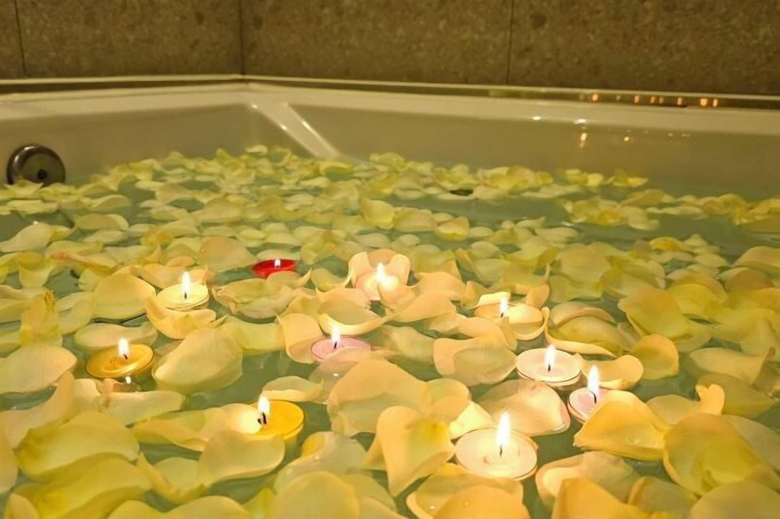 Uma banheira cheia de água e pétalas de rosa, com velas sobre a superfície.
