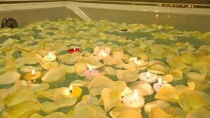 Una bañera llena de agua y pétalos de rosa, con velas sobre la superficie.