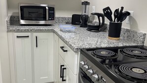 Eine Küche mit weißen Schränken, einem schwarzen Herd, einer Mikrowelle, einem Mixer und einer Kaffeemaschine.