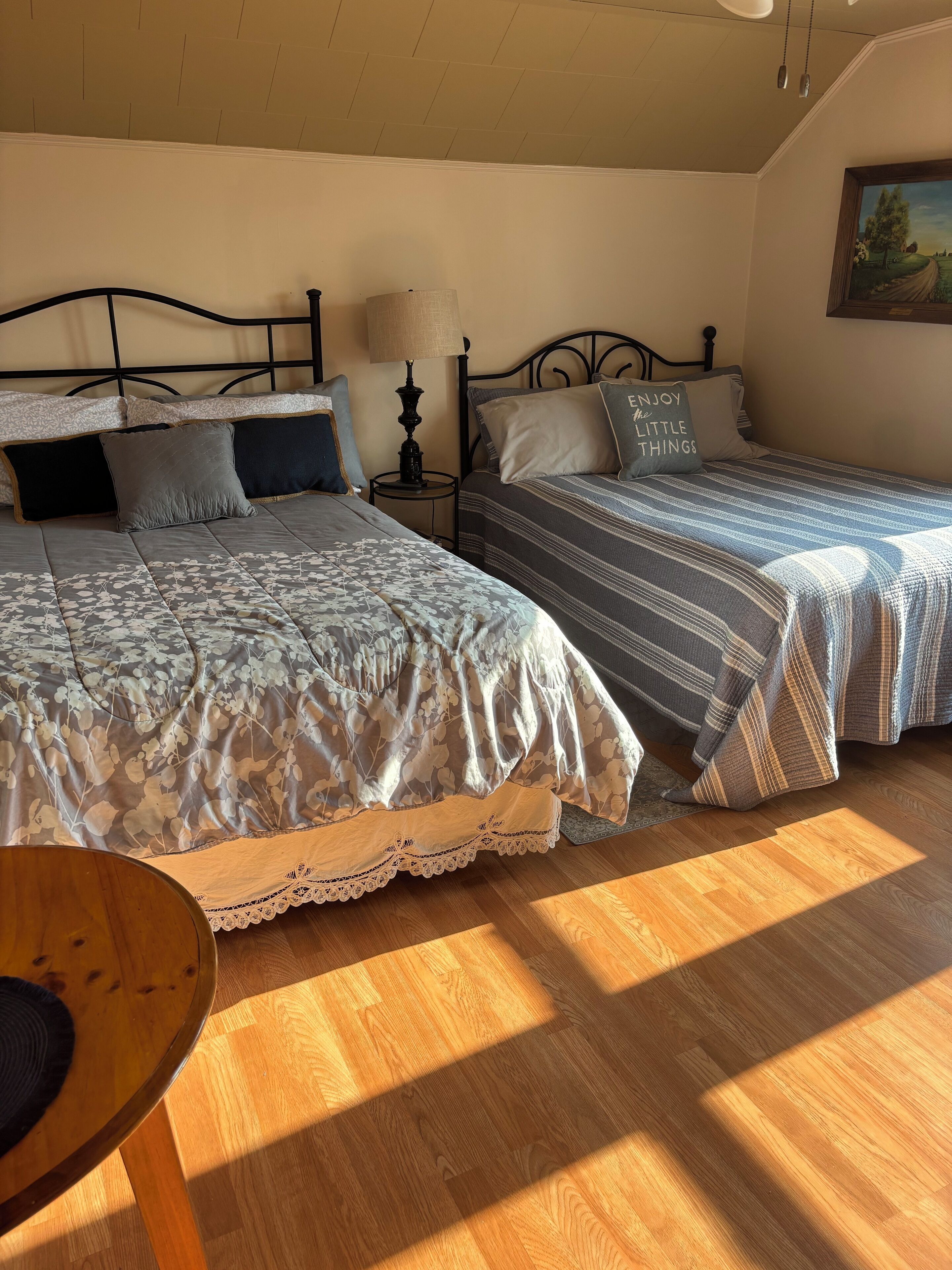 A bedroom with two beds, a small table, and a painting on the wall.