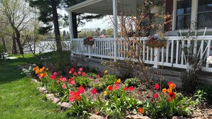 A house with a porch, a garden with colorful flowers, and a lake in the background.