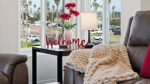A modern living room with a leather couch, a wooden coffee table, and a view of palm trees and cars through large windows. - Stunning beach home located between bay and beach w/ Ocean View Patio (San Diego)