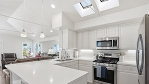 A modern kitchen with white cabinetry, stainless steel appliances, a central island, and pendant lighting. - Stunning beach home located between bay and beach w/ Ocean View Patio (San Diego)