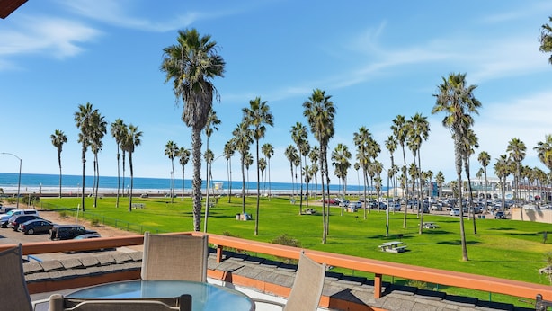 A balcony with a view of a beach, palm trees, and a parking lot. - Stunning beach home located between bay and beach w/ Ocean View Patio (San Diego)