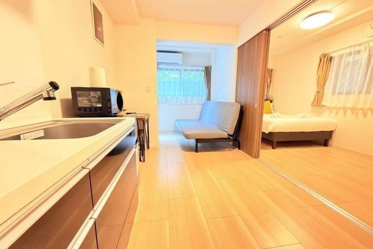 Une petite pièce comprenant un coin cuisine, un lit, une chaise et une fenêtre avec des rideaux.