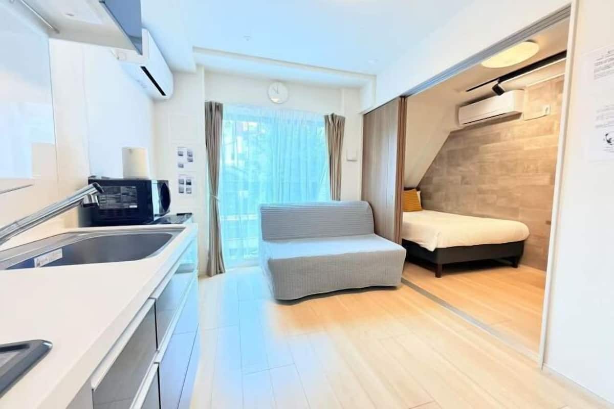Une pièce compacte comprenant un coin cuisine, un canapé, un lit et une fenêtre avec des rideaux.