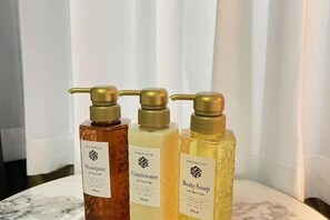 Three bottles of shampoo, conditioner, and body soap on a marble surface.