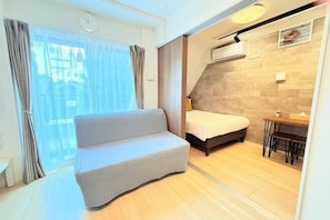A modern hotel room with a sofa, a bed, a small table, and a view of the city.
