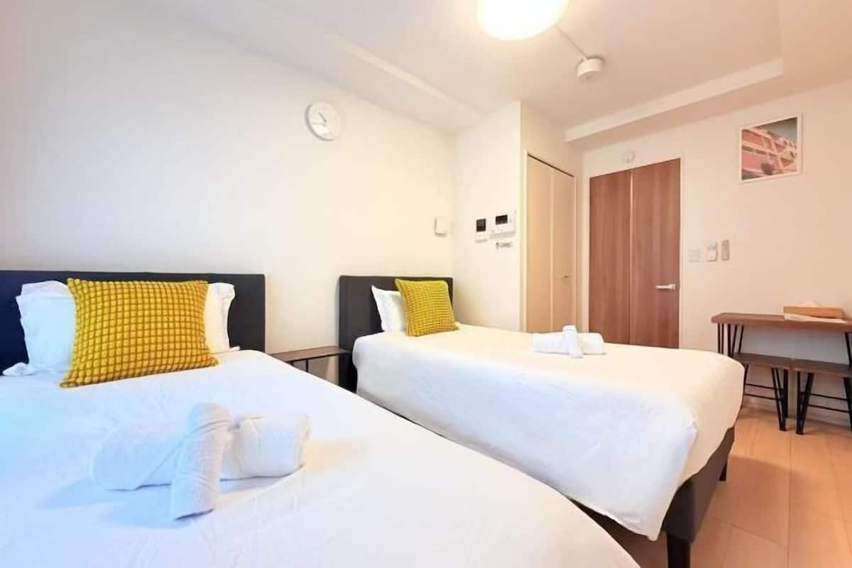 Une chambre d’hôtel avec deux lits, un bureau, une chaise, une horloge et une porte.