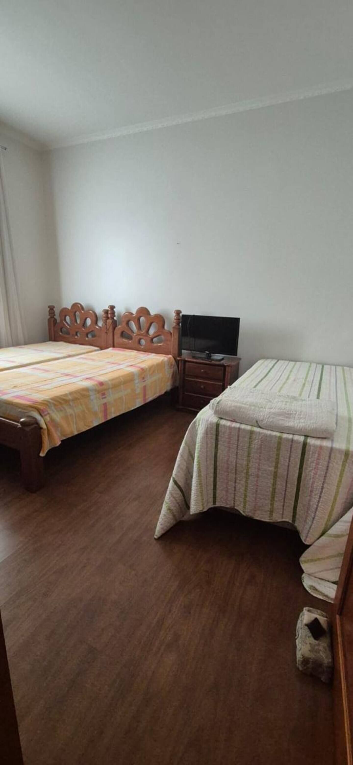 A bedroom with two wooden beds, a television on a wooden stand, and a small wooden nightstand.