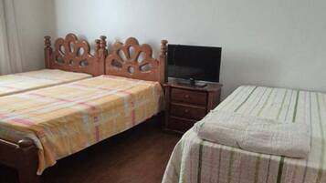 A bedroom with two wooden beds, a television on a wooden stand, and a small wooden nightstand.