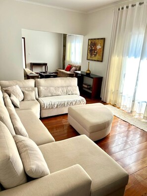 A modern living room with a sectional sofa, a small ottoman, and a side table. - Family Home for Graduations (Alfenas)