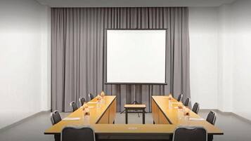 Ein Konferenzraum mit einem langen Tisch, Stühlen, einer Projektionsfläche und einer Whiteboard-Tafel.