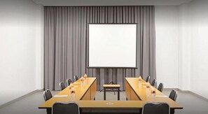 Una sala de conferències amb una taula llarga, cadires, una pantalla de projector i una pissarra.