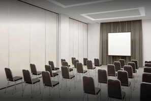A conference room with rows of chairs facing a blank projection screen. - Amaris Hotel Manado (Wenang)