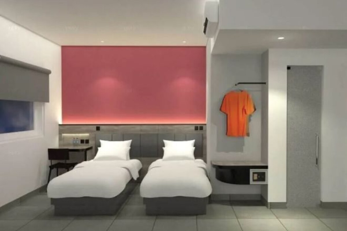 Habitació d'hotel moderna amb dos llits, una paret d'accent rosa i una taula petita amb una cadira.