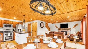 A spacious kitchen with wooden cabinets, a dining area with a wooden table set for four, and a living room with a fireplace and leather sofa.