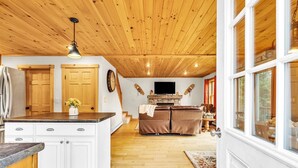 A spacious living area with a wooden ceiling, a central fireplace, and a television.