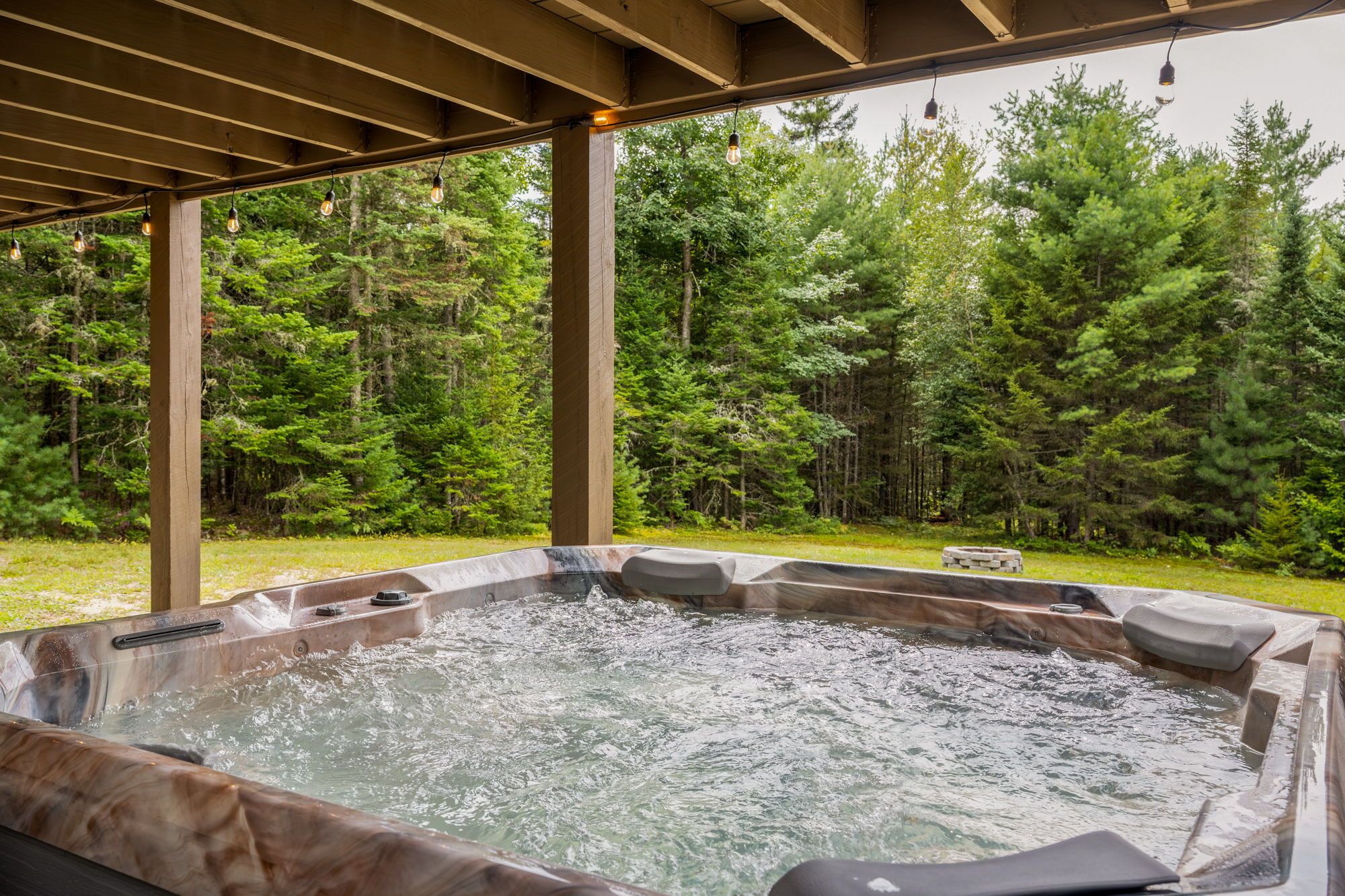 A hot tub with a wooden pergola overhead, surrounded by a forested area.