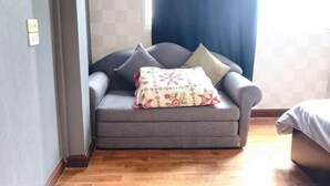 A room with a grey sofa, a floral throw pillow, and a bed with a white cover. - 24 Hostel Donmuang (Bangkok)