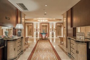 Un vestíbulo de hotel con una araña central, una recepción y una alfombra roja que conduce a la entrada.