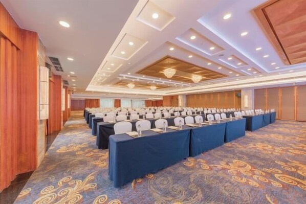 Un salón de conferencias con filas de mesas y sillas, alfombra estampada y diseño de techo de madera.