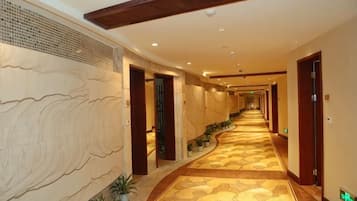 Un couloir d’hôtel avec un tapis à motifs, des portes en bois et un mur à la texture particulière.