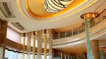 Un atrio de varios niveles con una imponente escalera, columnas grandes y una lámpara de araña moderna.