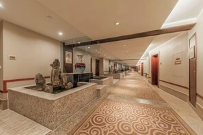 Un pasillo de hotel con alfombra estampada, una zona de recepción con un florero y un largo pasillo con puertas.