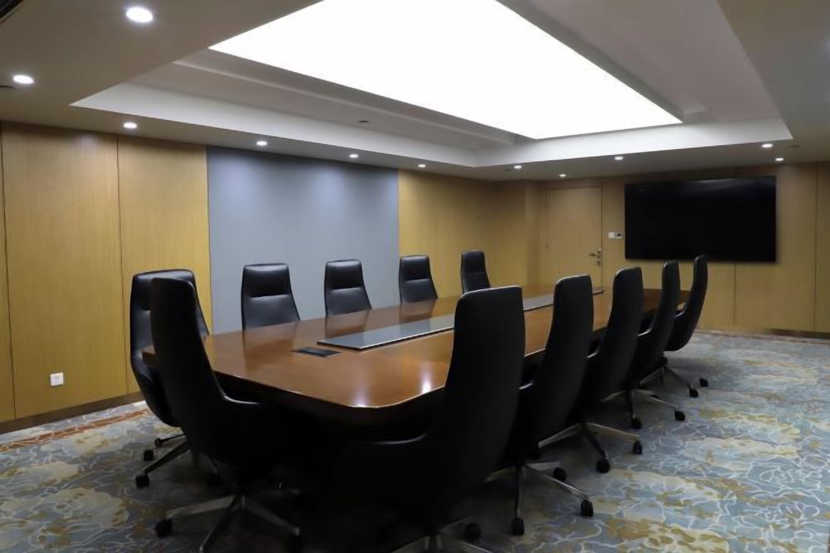 Un salón de conferencias con una mesa larga, sillas negras, un televisor de pantalla plana y una alfombra estampada.