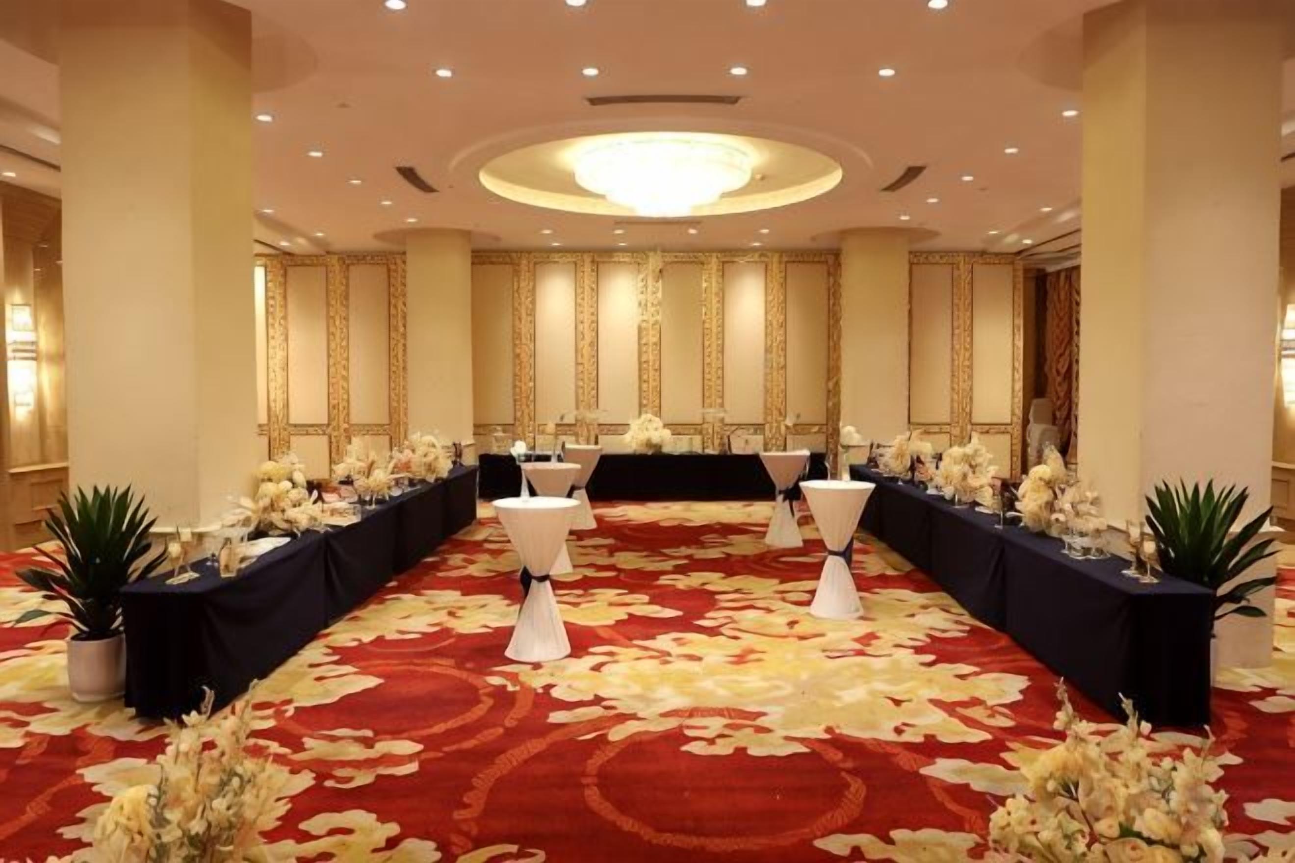 A banquet hall with a long table set for a formal event, flanked by white chairs and floral arrangements.