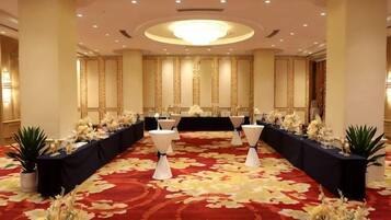A banquet hall with a long table set for a formal event, flanked by white chairs and floral arrangements.