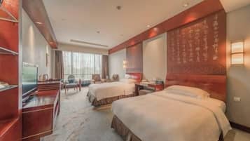 Habitación de hotel con dos camas, un escritorio, televisor y una ventana grande con cortinas.